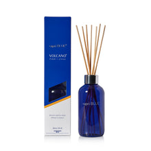 A reed diffuser bottle in cobalt blue glass with natural reed sticks, standing next to its blue and white packaging box labeled 'capri BLUE' and 'VOLCANO'.