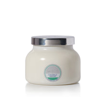 A white coconut santal scented candle in a cream-colored jar with a shiny silver lid, set against a plain white background.