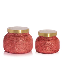 Two red glitter scented candle jars with gold lids on a white background