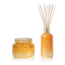 A scented candle jar and a diffuser bottle with gold caps on a white background