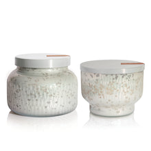 Two glass scented candle jars with speckled patterns and white lids on a white background