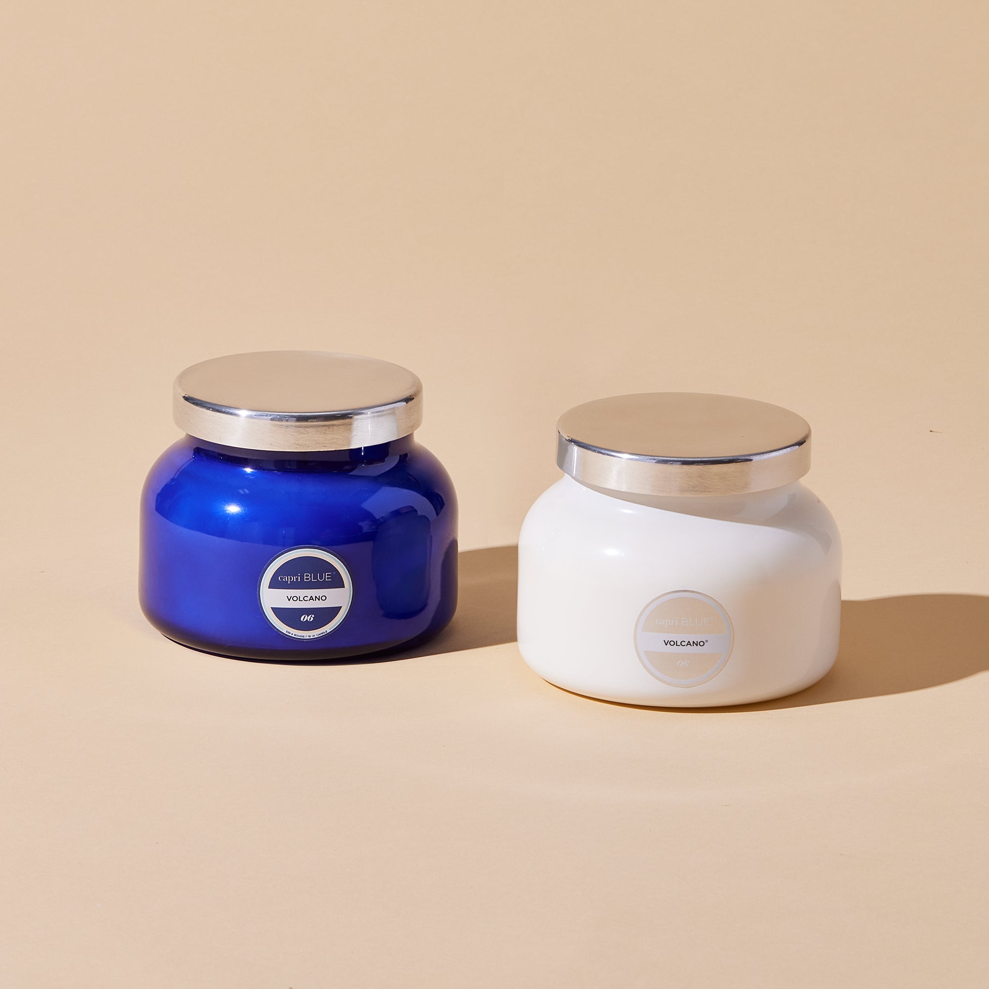 Two jars, one blue and one white, with silver lids on a beige background.