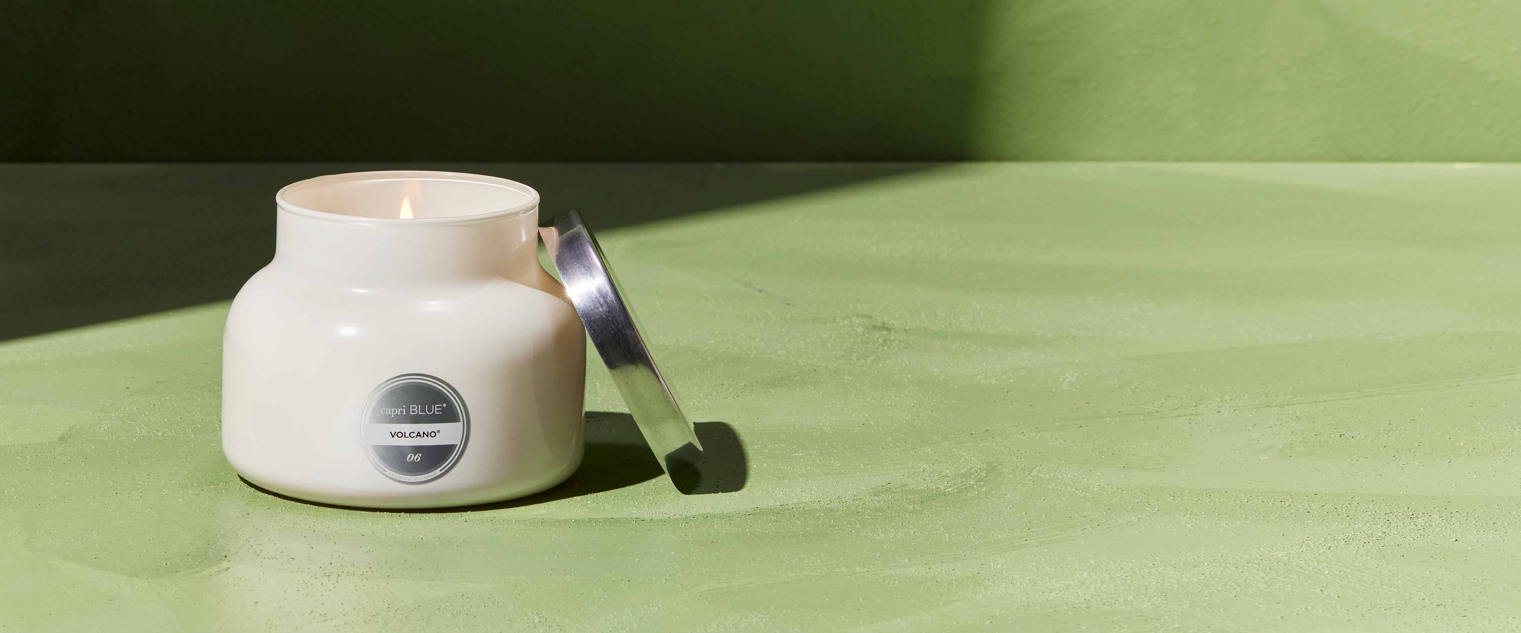 White Signature Volcano candle in a jar with a label on a green surface
