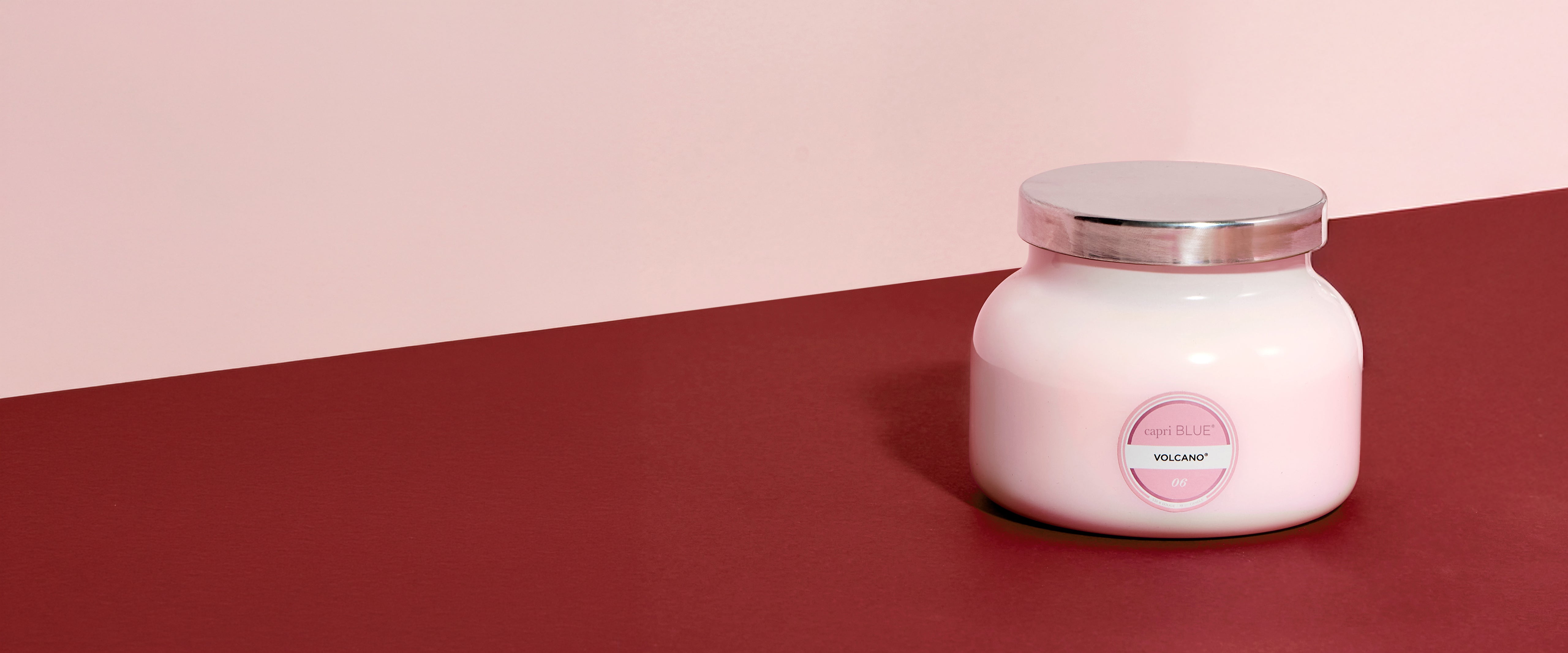Pink candle jar with a label on a two-tone pink and red background