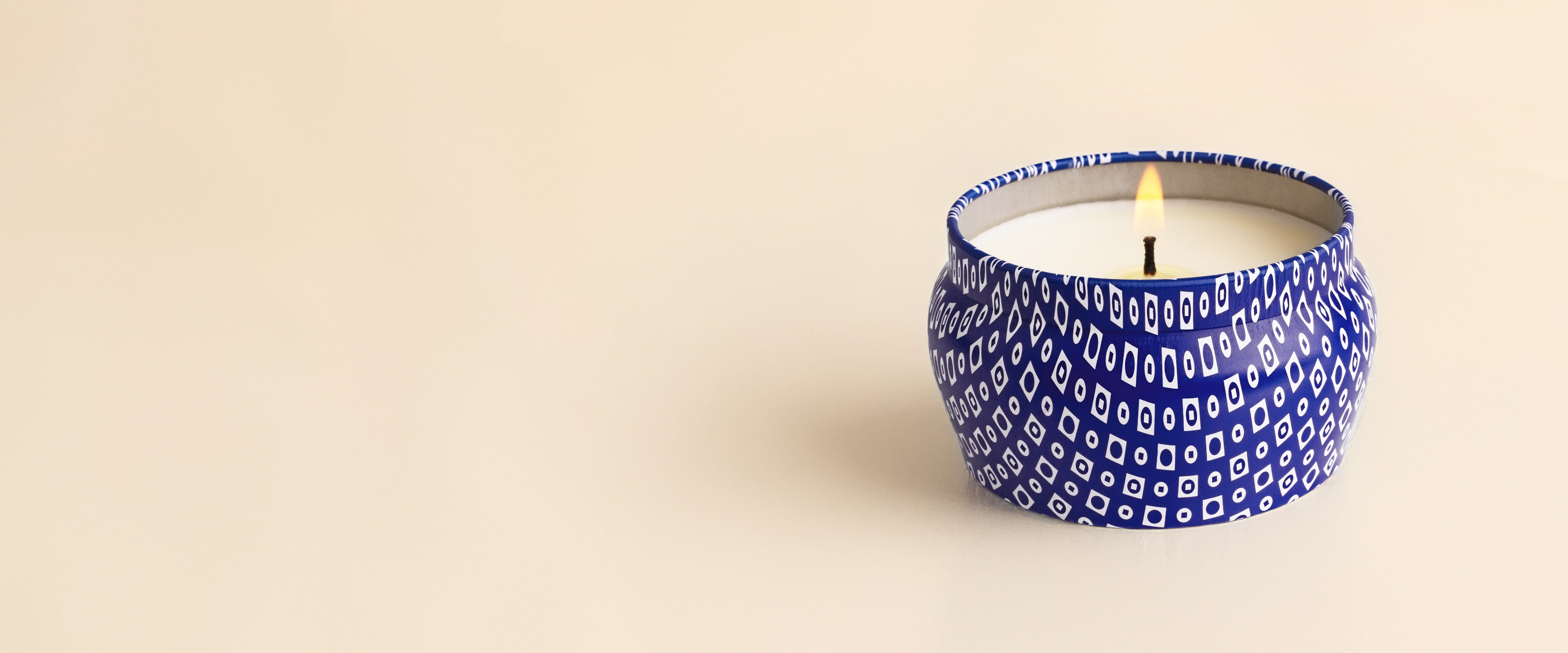 Candle in a blue patterned container on a beige background
