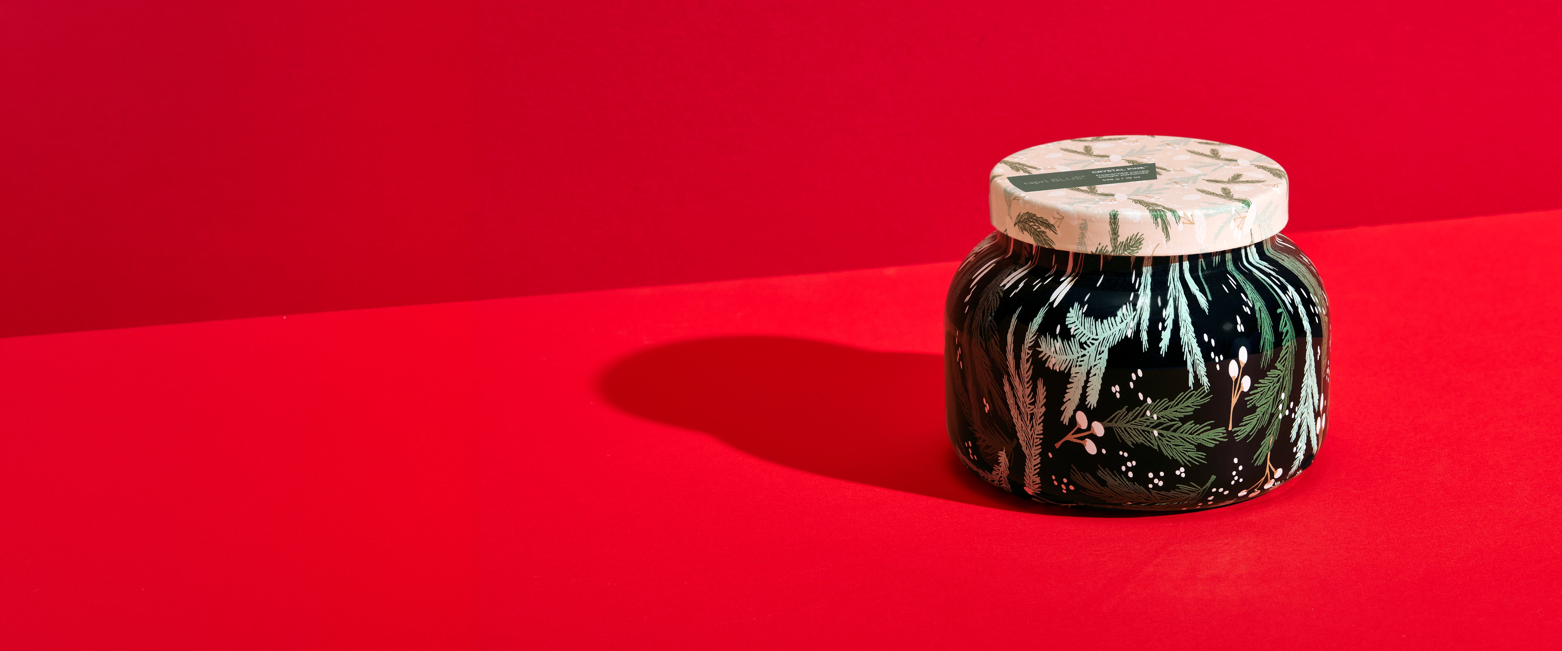 A small decorative jar with a marbled black and white lid and a dark body featuring green leaf patterns, set against a solid red background.