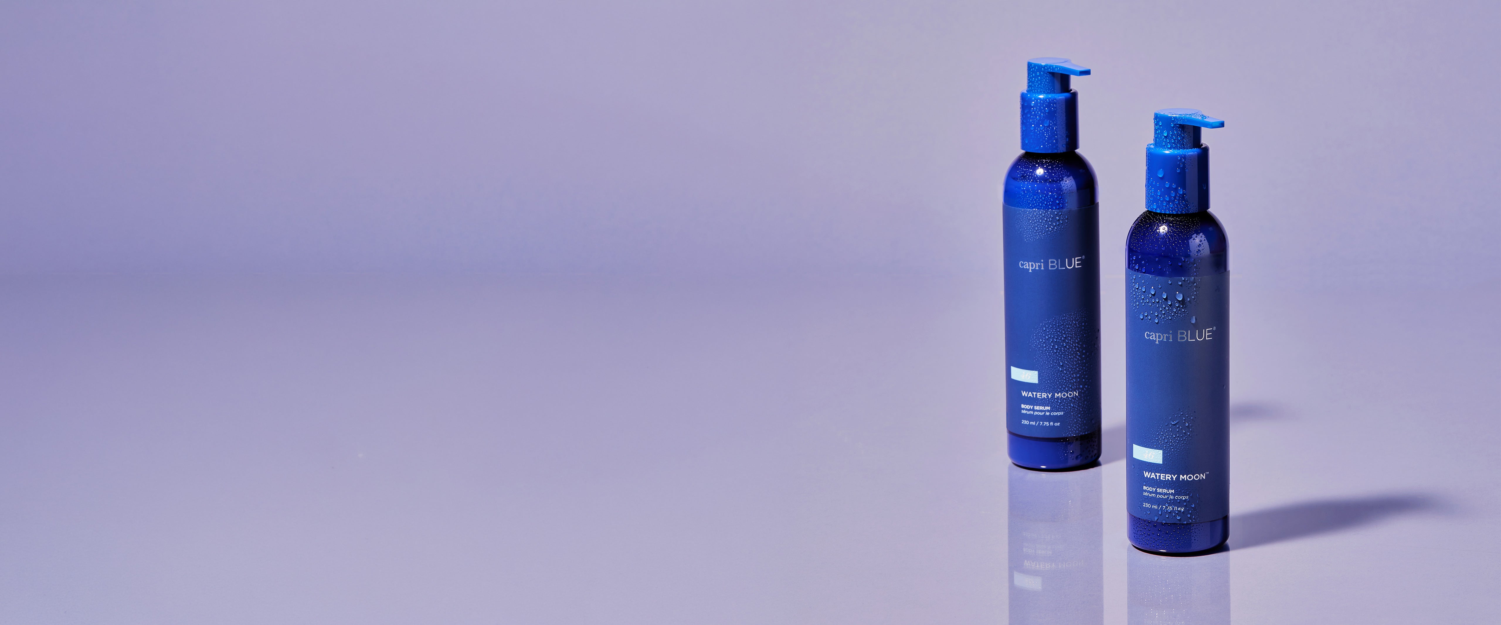 Two dark blue pump bottles with blue caps, standing on a reflective light purple surface against a matching purple background.