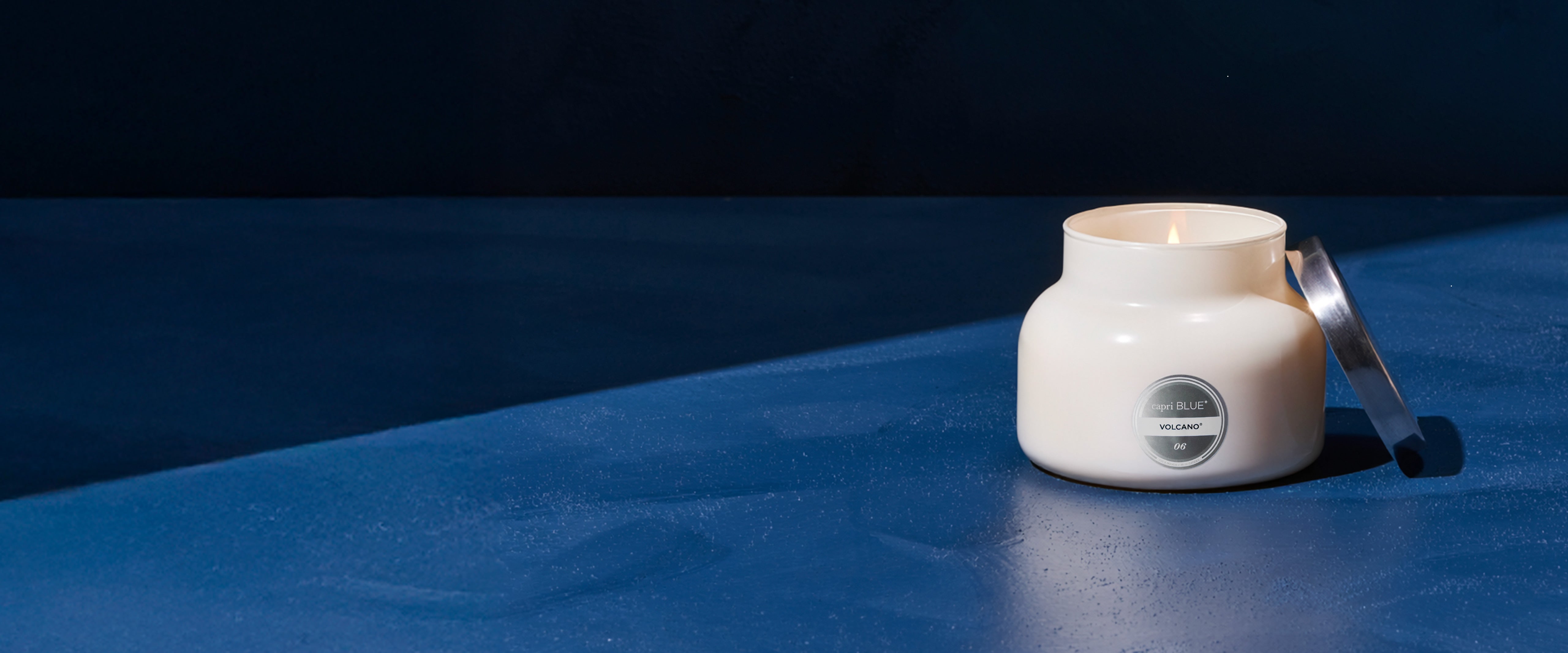 White Volcano Signature jar with a candle on a blue surface