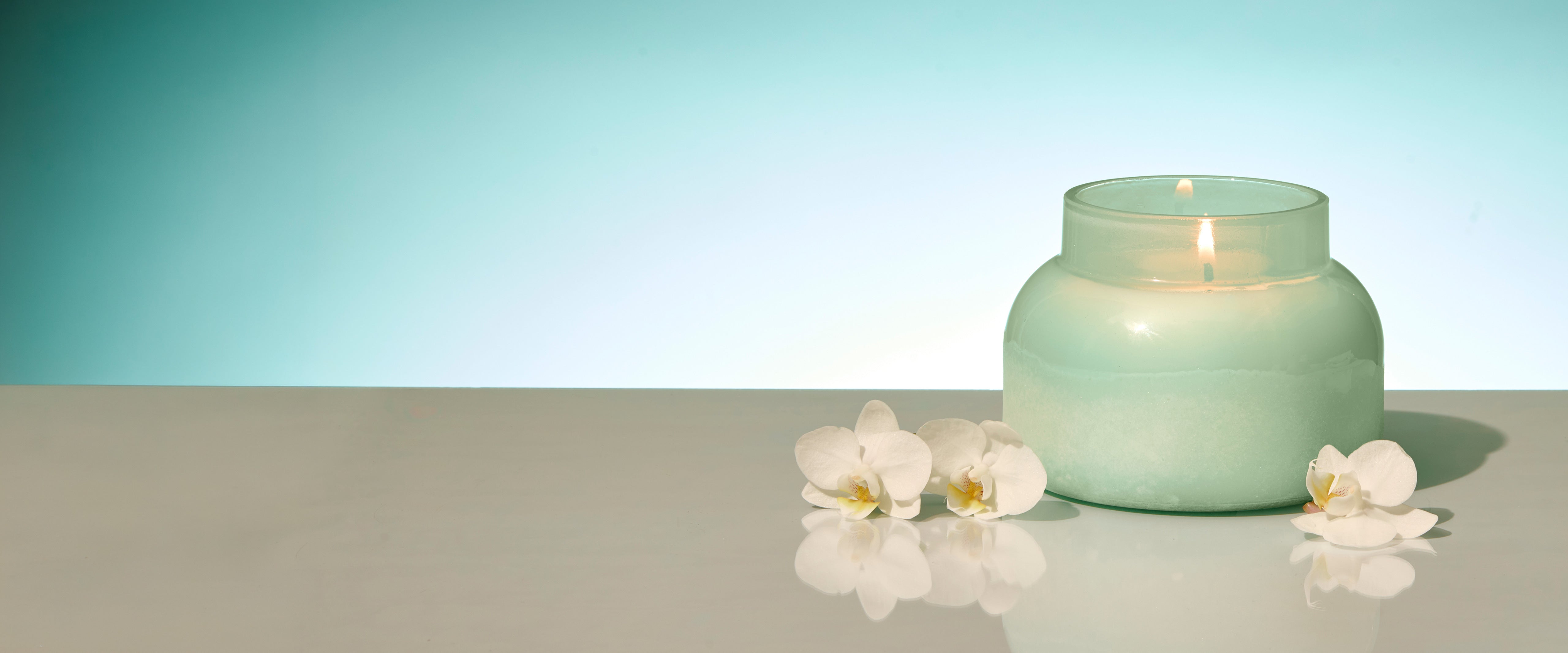 Green candle and white flowers on a reflective surface with a gradient background