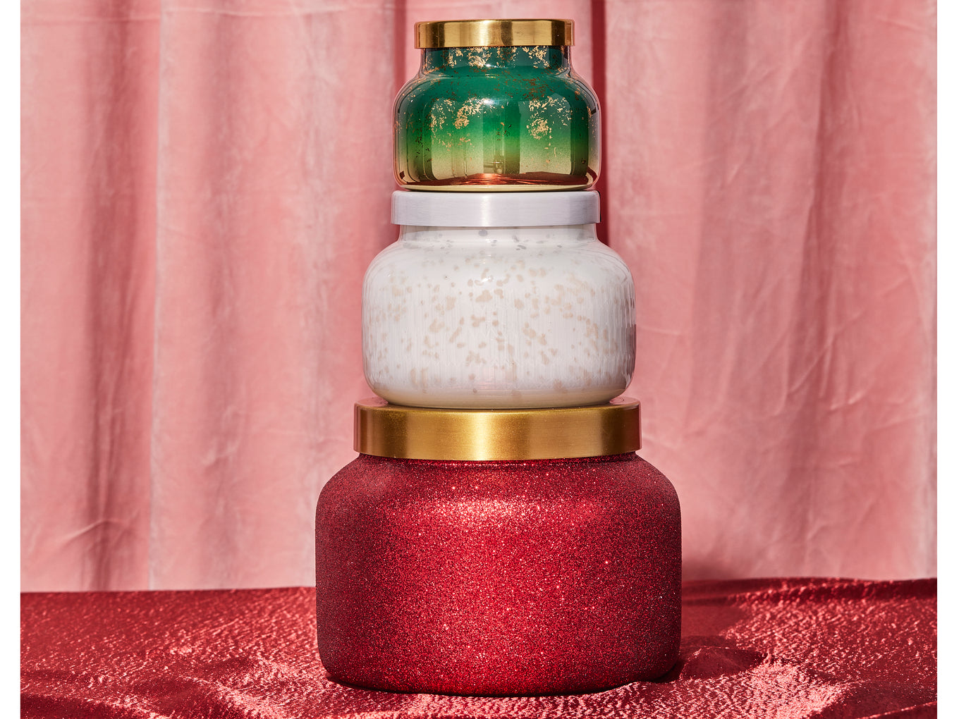 Stack of decorative candles with different colored bases on a pink background