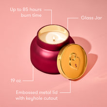 Red candle with gold lid on a pink background, showing features like burn time and weight.